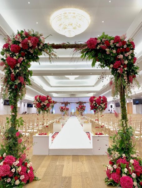 Floral wedding arch with pink roses, leading to a white aisle and decorated venue.