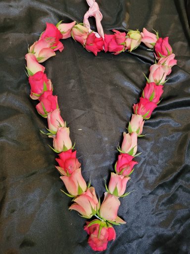 Heart-shaped arrangement of pink roses with a small decorative figure.