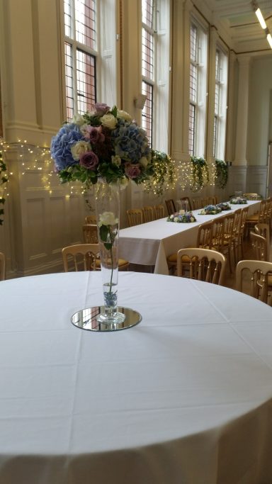 A round table set with a white cloth and a floral centrepiece in a banquet hall.