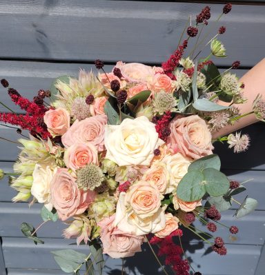 A bouquet featuring pale pink roses, red foliage, and various garden flowers.