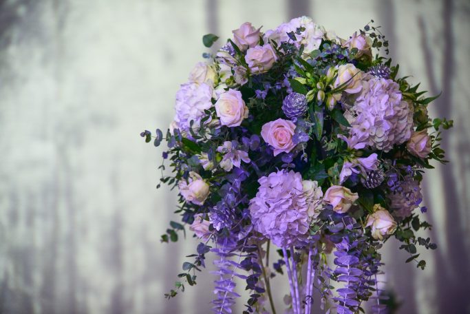 A bouquet of pink and purple flowers with green foliage on a blurred grey background.