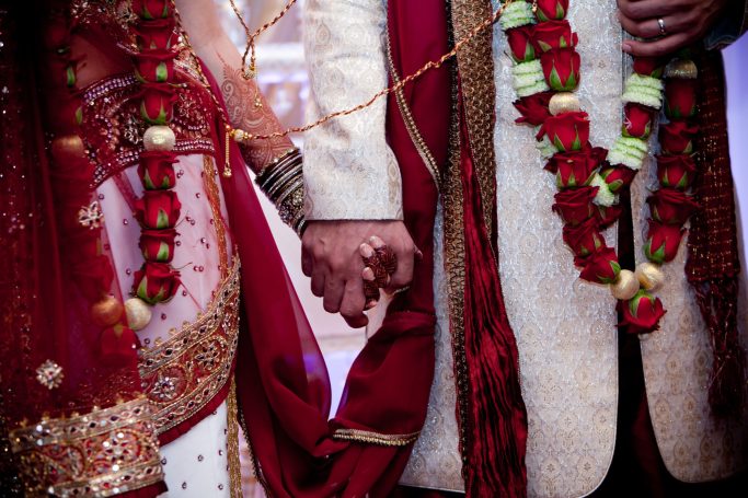 Two individuals in traditional attire holding hands, adorned with floral garlands.