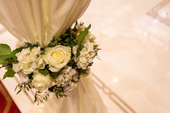 A bouquet of white roses and greenery next to a draped fabric.