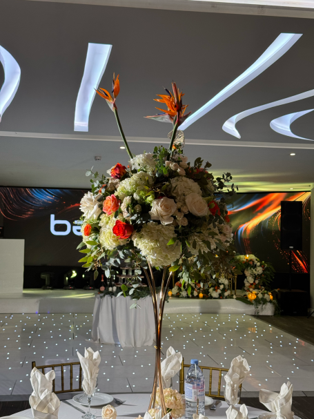 Tall floral arrangement with orange and white flowers in an elegant venue setting.