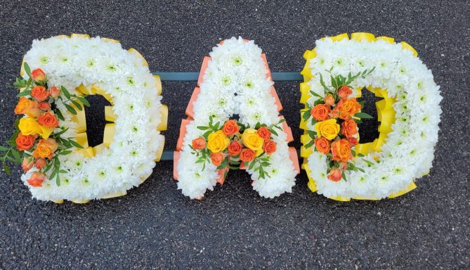 Floral arrangement spelling "DAD" in white and orange flowers.