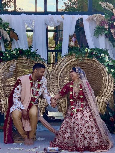 A couple in traditional wedding attire sitting together, surrounded by floral decorations.