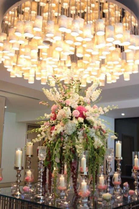 Elaborate floral arrangement with candles, under a bright chandelier.