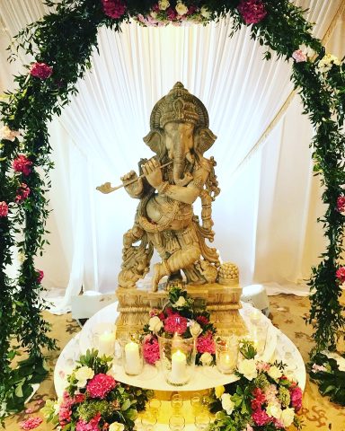 A decorative shrine featuring a Ganesh statue, surrounded by flowers and candles.