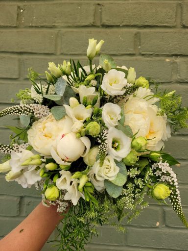 A hand holding a bouquet of white and green flowers with delicate foliage.