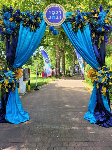 Decorative archway with blue and yellow drapes, adorned with flowers, leading to a path.