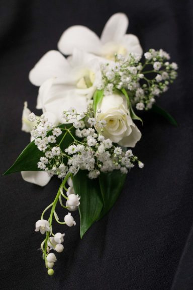 White rose and orchids arranged with baby’s breath on dark fabric.