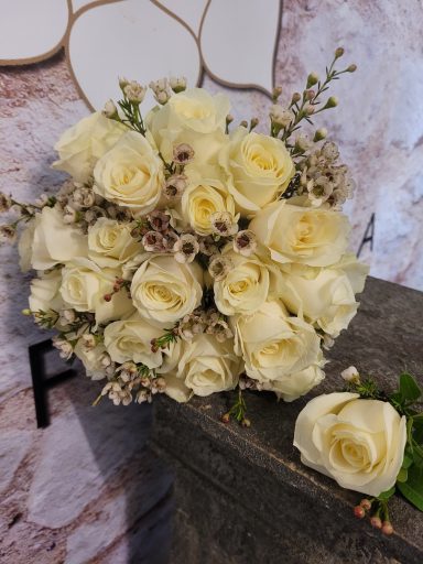 A bouquet of cream roses with delicate filler flowers, resting on a textured surface.