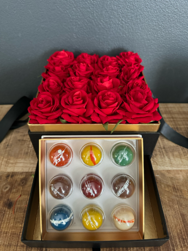 A black box with red roses on top and a selection of colourful chocolates inside.