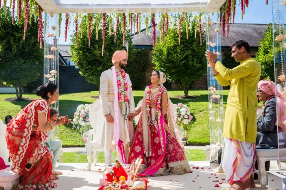 A couple in traditional attire during a wedding ceremony, surrounded by family and decorations.