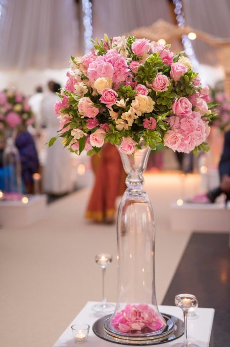 Tall vase filled with pink and white flowers, surrounded by candles and decorations.