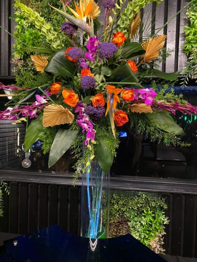 Vibrant floral arrangement featuring orange, purple, and pink flowers with green foliage.
