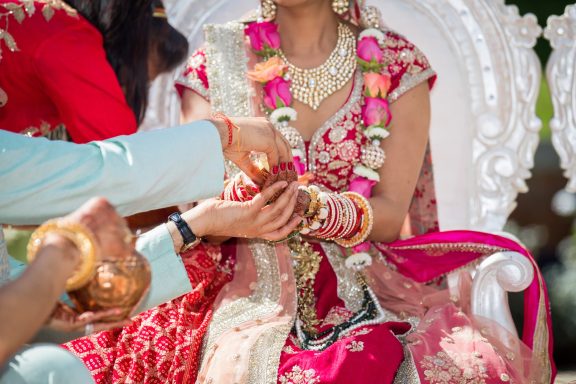 Bride in ornate attire adorned with floral garlands during a traditional ceremony.