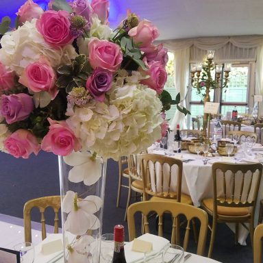Tall floral arrangement with pink roses and white hydrangeas on a banquet table setting.