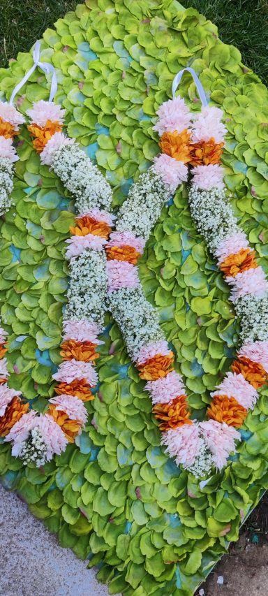 Two floral garlands with orange, pink, and white flowers on a green backdrop.