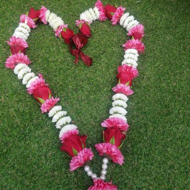 A heart-shaped floral arrangement with pink and white flowers on green grass.