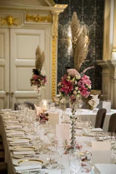 Elegant dining table set with floral centrepieces and glassware in a lavish interior.