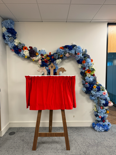 A decorated wall with blue and colourful flowers beside a red-draped display stand.