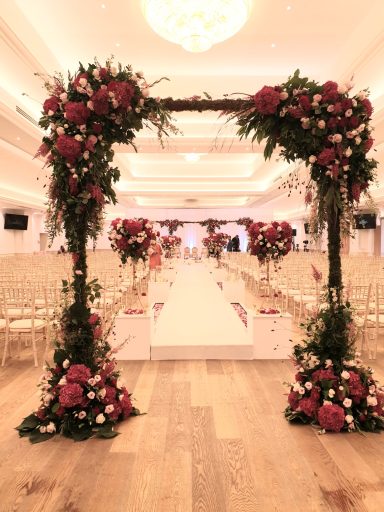 Floral archway leading to a decorated aisle in a wedding venue.