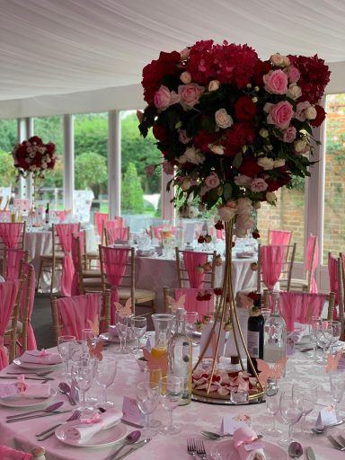 A beautifully arranged table setting with a tall floral centerpiece and pink decorations.