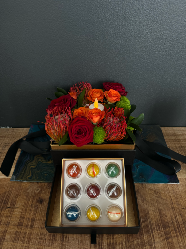 A bouquet of red and orange flowers beside a box of assorted chocolates.