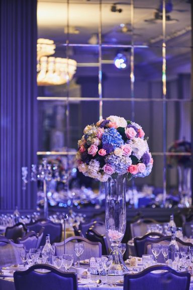 Elegant table setting with a tall flower arrangement and soft purple lighting.
