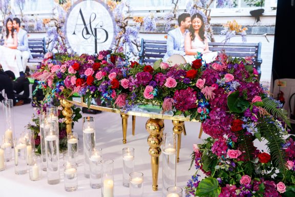 Lavish floral arrangement in vibrant colours with candles and a backdrop featuring a couple.