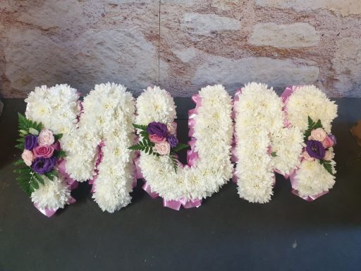 Floral arrangement spelling "MUM" with white and purple flowers.