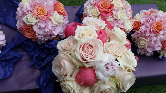 A vibrant arrangement of pink and cream roses and peonies on a purple surface.