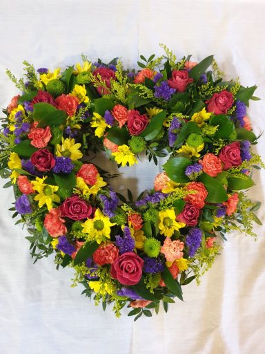 Heart-shaped floral arrangement with vibrant mixed flowers and greenery.