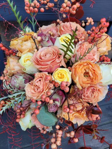 A bouquet of soft peach and yellow roses with foliage and berries.