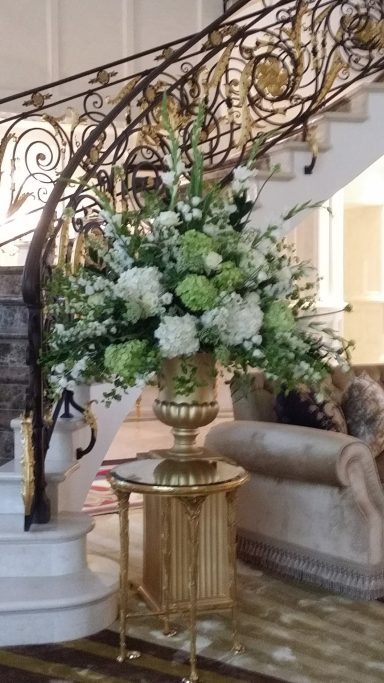A grand floral arrangement in a gold vase beside an elegant staircase.