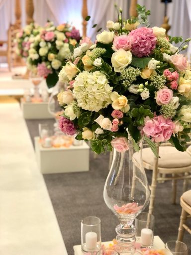 Floral arrangements with roses, hydrangeas, and greenery in a wedding setting.