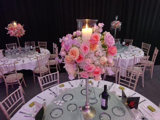 Elegant floral centrepieces on round tables with candlelight at a formal event.