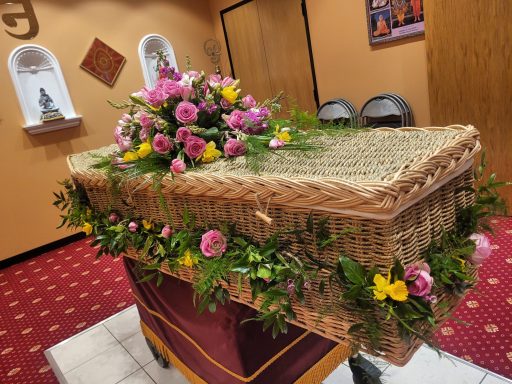 A decorated wicker casket adorned with vibrant flowers in a ceremonial setting.