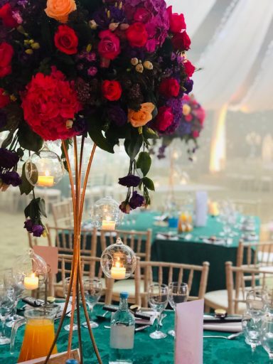 Flower arrangements on tall stands above elegantly set dining tables at a festive event.