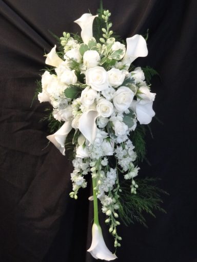 Bouquet of white roses and calla lilies with greenery against a dark background.