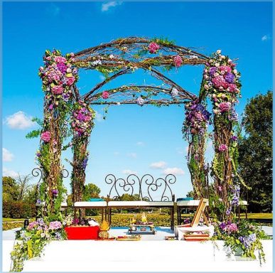 Floral wedding arch adorned with purple flowers and greenery against a blue sky.