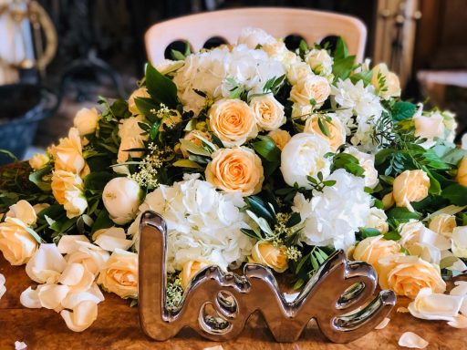 A floral arrangement with white and yellow roses, complemented by greenery and the word "love."