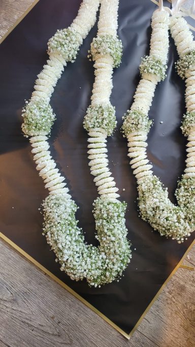 Three decorative garlands made of white flowers and green leaves on a dark surface.