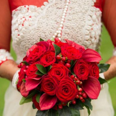 A bouquet of red roses and pink calla lilies held by a person in traditional attire.