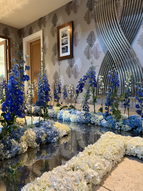 Delphiniums and white flowers arranged decoratively on a reflective floor in a stylish room.