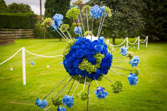 A spherical floral arrangement in blue and green, set on a grassy area.