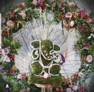 A moss-covered Ganesh statue surrounded by colourful floral decorations.